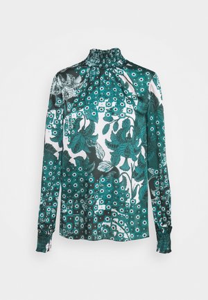 Blouse à manches longues avec motif floral et feuillage bleu-vert et blanc, encolure haute froncée et poignets froncés, présentée sur fond blanc.