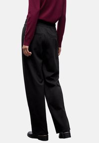 Pantalon noir en tissu lisse avec une coupe décontractée, taille élastique, poches latérales et détails distinctifs au niveau des poches arrière.