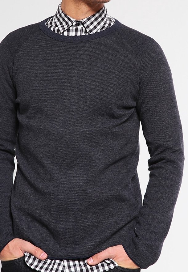 Maglione grigio scuro con maniche raglan e un lavorato a maglia testurizzato, indossato sopra una camicia a scacchi bianco e nero con colletto rigido.