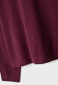 Bordo pulover s glatkom, mekanom teksturom, zaobljenim rubom i minimalnim šavovima, s čistim, jednostavnim dizajnom.
