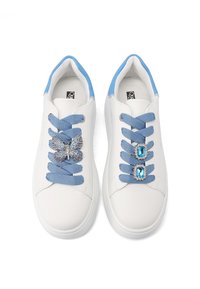 Sneakers bianchi con dettagli blu, dotati di lacci blu, una farfalla decorata con gioielli e due elementi decorativi con gemme blu sulla scarpa destra.
