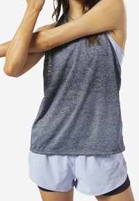 Šedý sportovní top s texturovaným povrchem, kombinovaný s světle modrými kraťasy. Top má volný střih a kulatý výstřih.