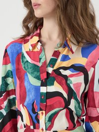 Colorful button-up shirt featuring a blend of abstract patterns in red, blue, green, and cream. Long sleeves with a relaxed fit.