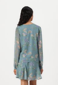 Robe en chiffon légère de couleur bleu clair avec un motif floral, dotée de longues manches, d'épaules froncées et d'un ourlet évasé. Présente de délicates accents floraux multicolores.