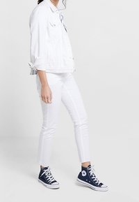 Chaqueta de mezclilla blanca, camisa azul clara, jeans ajustados blancos y zapatillas altas navy con suelas y cordones blancos. Tela de algodón, diseño casual.