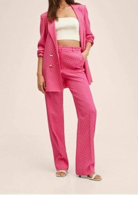 Traje rosa con estampado de lunares que incluye una americana ajustada con botones dobles y pantalones de pierna ancha. El material tiene una textura suave.