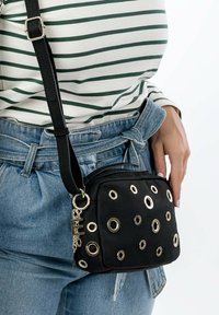 Borsa a tracolla in tessuto nero con decorazioni in occhio di bue color oro e un portachiavi decorativo. Forma quadrata con tracolla regolabile.