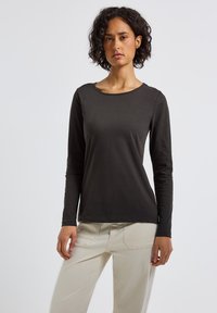 T-shirt noir à manches longues avec un col rond et une texture lisse et douce, associé à un pantalon beige clair.