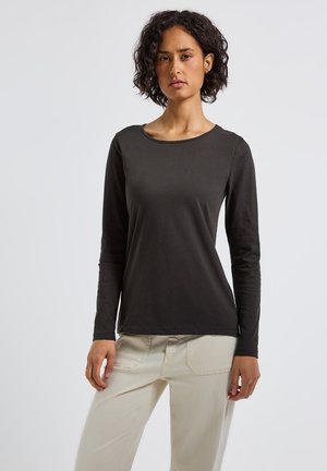 T-shirt noir à manches longues avec un col rond et une texture lisse et douce, associé à un pantalon beige clair.