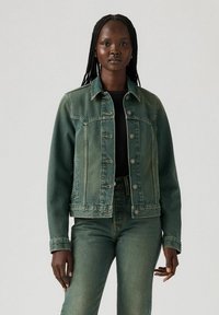 Green denim jacket with a button-up front, two chest pockets, and a slightly faded texture. Paired with matching green denim pants.
