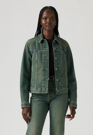 Giacca di jeans verde con chiusura a bottoni, due tasche sul petto e una texture leggermente sbiadita. Abbinata a pantaloni di jeans verdi coordinati.