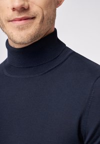 Marineblauer Rollkragenpullover aus feinem Strickstoff, mit einem gerippten Kragen und glatter Textur. Nahaufnahme, die den Ausschnitt des Kleidungsstücks hervorhebt.