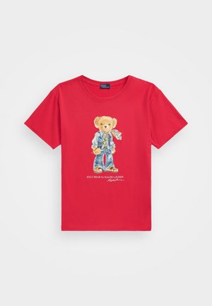 Czerwona koszulka z krótkim rękawem z grafiką misia w dżinsach, kurtce i szaliku oraz tekstem "Polo Bear by Ralph Lauren" poniżej.