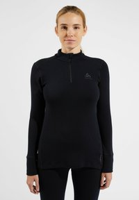 Schwarz langärmliges Thermoshirt mit Reißverschlusskragen, das über ein tailliertes Design und ein Logo auf der Brust verfügt. Hergestellt aus einem glatten, dehnbaren Material.