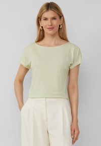 Hellgrünes, kurzärmliges Oberteil mit einem Bootsausschnitt, aus einem weichen, strukturierten Material gefertigt. Kombiniert mit cremefarbenen Hosen für einen Kontrast.