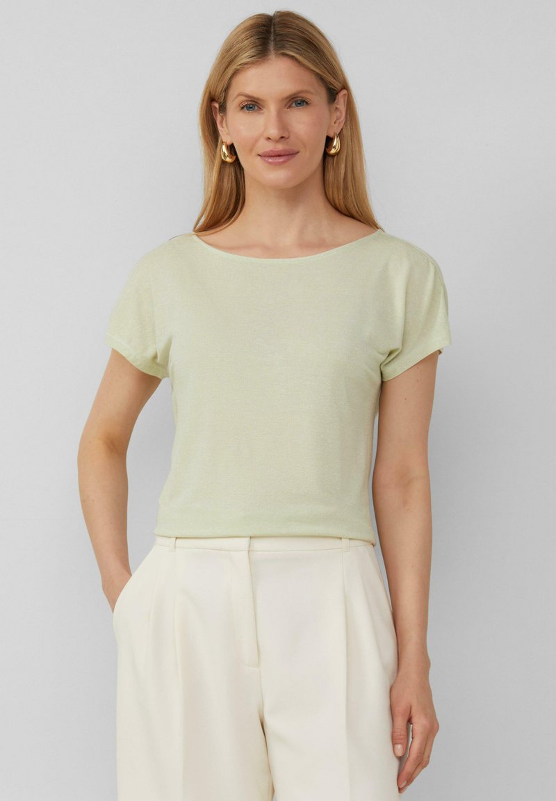 Hellgrünes, kurzärmliges Oberteil mit einem Bootsausschnitt, aus einem weichen, strukturierten Material gefertigt. Kombiniert mit cremefarbenen Hosen für einen Kontrast.