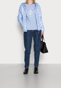 Chaqueta acolchada azul clara con capucha, combinada con un sudadera azul clara con un estampado náutico, jeans azules y botas negras hasta el tobillo. Bolso negro.