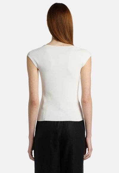 Top bianco aderente con maniche a cappuccio, texture a maglia liscia e scollo rotondo. Abbinato a pantaloni neri a gamba larga, che mettono in evidenza una silhouette elegante.