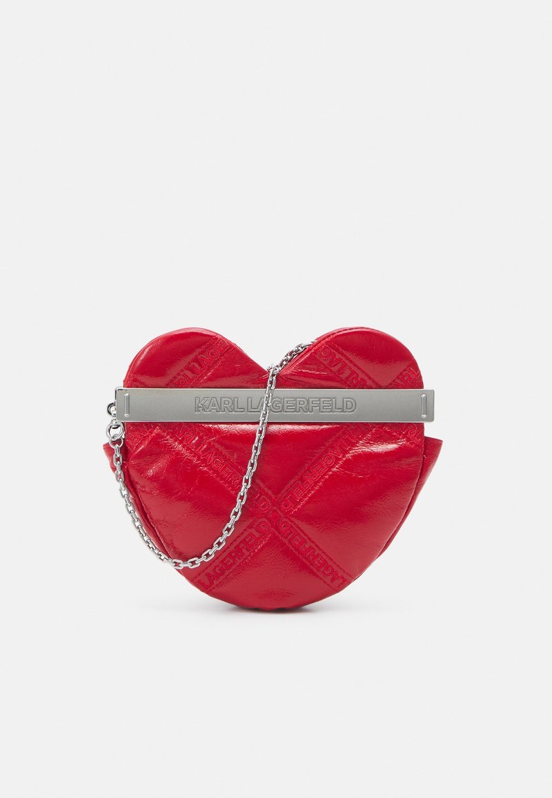 Punainen sydämenmuotoinen käsilaukku, joka on valmistettu kiiltävästä materiaalista. Laukussa on hopeinen metallikahva, jossa on kohokuvioitu nimi "KARL LAGERFELD".