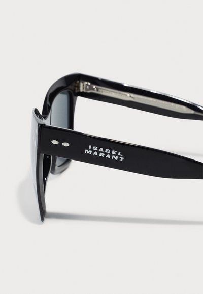 Black sunglasses with wide frames, tinted lenses, and an engraved logo on the arm. Features solid texture and sleek design.