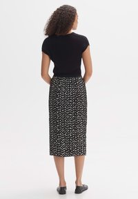 Top corto a maniche corte nero a coste abbinato a una gonna midi con motivo in bianco e nero, caratterizzata da disegni rettangolari, indossato con scarpe basse nere.