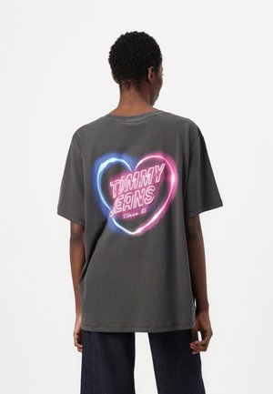 T-shirt oversized gris avec un col rond, arborant un graphique de cœur néon et le texte "TOMMY JEANS Since 85" au dos.