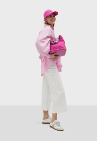 Rosa strukturierte Tragetasche mit einem kontrastierenden schwarz-weißen Tragegurt. Weiße weit geschnittene Hose, pinke oversized Bluse und beigefarbene Sneakers.