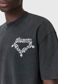 Musthave musta puuvillane T-särk ümmarguse kaelusega. Rinnal on valge graafika ketist ja südame aktsentidest, luues kontrastse disaini.
