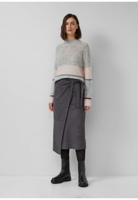 Hellgrauer gestreifter Pullover mit rosa und grauen Streifen; kombiniert mit einem grauen Wickelrock und schwarzen Stiefeletten. Weiche Textur und lässiges Design.