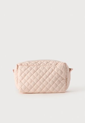 Sac en tissu matelassé rose pâle, à rayures verticales, avec une fermeture éclair sur le dessus et de petites boucles sur les côtés, sur un fond uni.