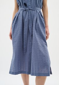 Rochie midi din bumbac albastru, cu dungi verticale, croi lejer, închidere cu nasturi, cordon la talie și slits laterale pentru un plus de mobilitate.