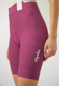 Korte sykkelshorts i dyp rosa med en jevn tekstur, med en hvit "Rapha"-logo og en sidelomme for oppbevaring.