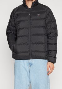 Svart puffjacka med dragkedja fram, hög krage och kviltad textur. Har en liten logotyp på övre vänstra sidan. Slim fit.