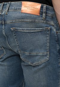 Πίσω όψη μπλε τζιν με ραμμένη τσέπη και καφέ δερμάτινη ετικέτα με την επιγραφή Marc O'Polo est. στη Στοκχόλμη.