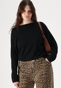 Zwarte, lange mouwen trui met een bootnek; gecombineerd met broek met luipaardprint met een knoopsluiting en voorzakken. Bruine schouderriem.