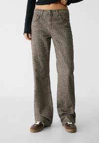 Džínsy s leopardím potiskem v tlumených hnědých tónech, s pěti kapsami, stříbrnými doplňky a zapínáním na knoflík, doplněné tmavými teniskami.