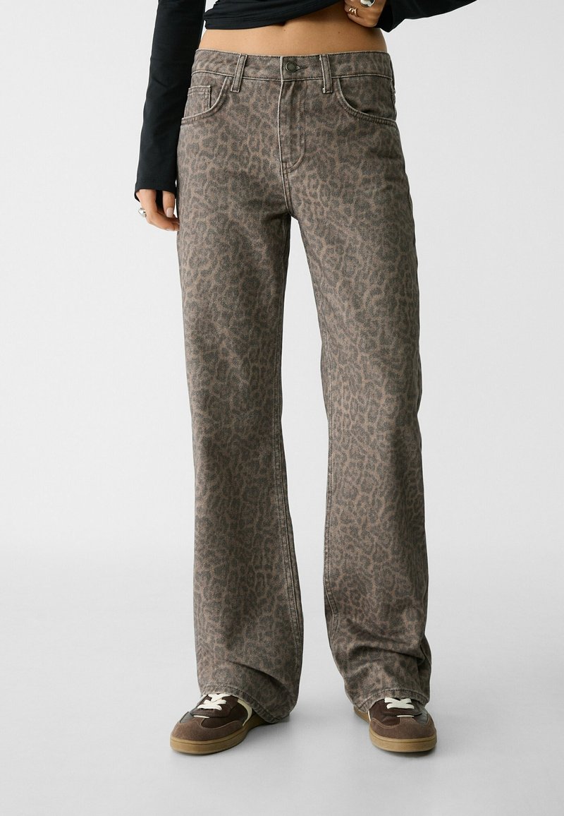 Džínsy s leopardím potiskem v tlumených hnědých tónech, s pěti kapsami, stříbrnými doplňky a zapínáním na knoflík, doplněné tmavými teniskami.