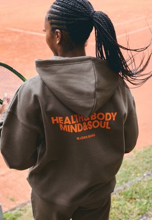 Barna kapucnis pulóver, elülső kenguruzsebbel, narancssárga szöveggel: "HEALTH&BODY MIND&SOUL" és "BJÖRN BORG" a hátsó oldalon. Teniszpálya látható.