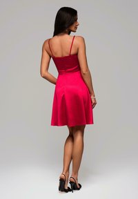 Robe sans manches fuchsia avec un corsage ajusté et une jupe évasée, dotée d'une fermeture éclair au dos. Portée avec des sandales à talons noirs.