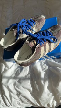 Adidas apavi ar brūna pleda auduma augšdaļu, zilām auklām un trim baltām svītrām, ar mīkstu balto oderi un oranžu zolīti.