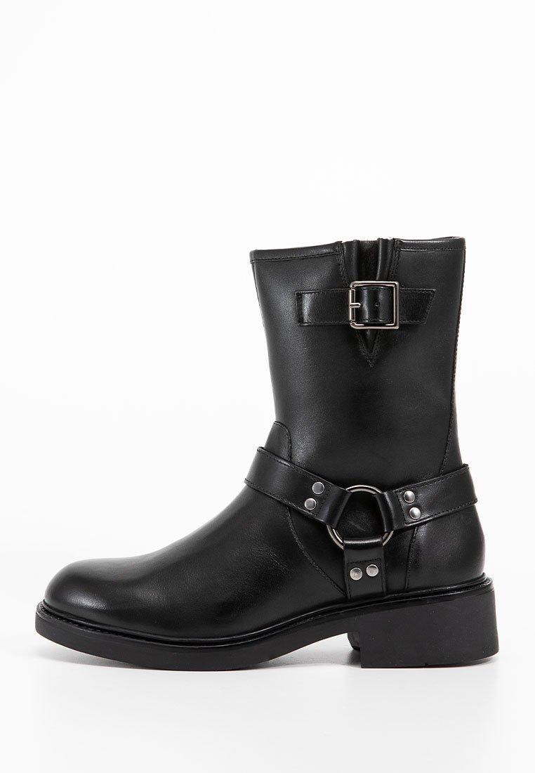 Schwarze Lederstiefel bis zur Wade mit dekorativem silbernem Schnallen- und Riemenakzent, niedrigem Absatz und runder Zehenform vor einem weißen Hintergrund.
