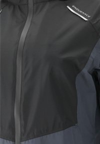 Svart och grå lättviktsjacka med dragkedja, texturerad tyg och reflekterande detaljer på axlarna. Endurance-logotyp synlig.
