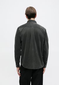 Szürke kordbársony ing gombos gallérral, hosszú ujjakkal és ívelt alsó szegéllyel. Jellemzője a függőleges bordás textúra és a gombos mandzsetta.