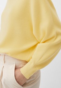 Geel gebreid sweater met lange mouwen, met een ribbeltextuur en een losse pasvorm, gecombineerd met lichtgekleurde broeken.