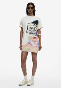 Ylihankinen t-paita mekko kerma värissä, jossa on värikäs painatus, rohkeaa tekstiä ja kuvastoja, sekä sileä ja pehmeä rakenne.