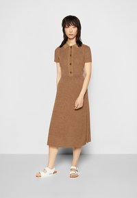 Vestido de malha canelada castanho com mangas curtas, com abertura de botões e saia rodada, combinado com sandálias brancas com fivelas.