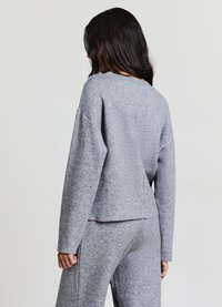 Grauer, strukturierter, gestrickter Pullover mit langen Ärmeln, rundem Ausschnitt und leicht verkürztem Saum. Kombiniert mit passenden grauen Hosen.