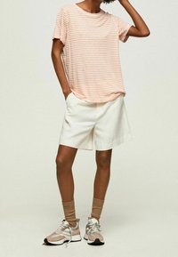 Gestreepte perzikkleurige t-shirt met korte mouwen, gecombineerd met witte, op maat gemaakte shorts. Draagt lichtroze en grijze sneakers, voorzien van beige enkelsokken.