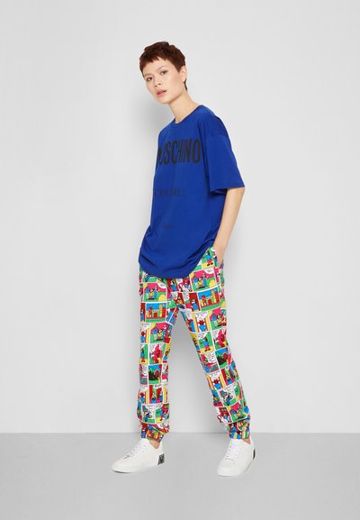 T-shirt oversized azul com estampa gráfica preta, combinado com calças coloridas estampadas com ilustrações em estilo de banda desenhada. Ténis brancos.