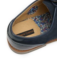 Blue suede shoe with brown leather accents. Interior features a multi-colored polka dot pattern. Label reads “Simon Carter.”